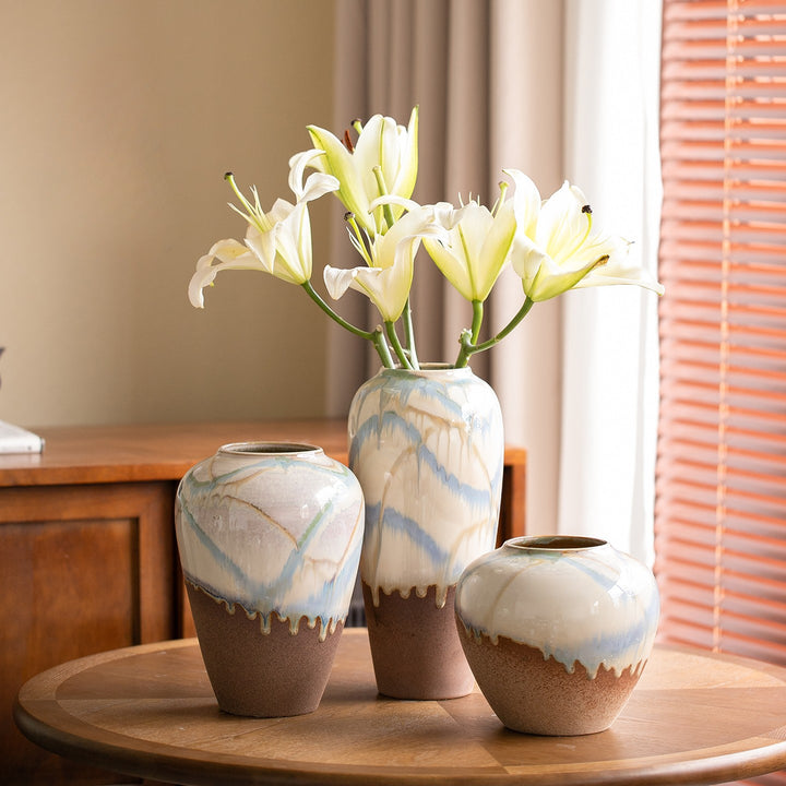 Three two-tone ceramic vases on a round wood table with open white lilies in the tall center vase