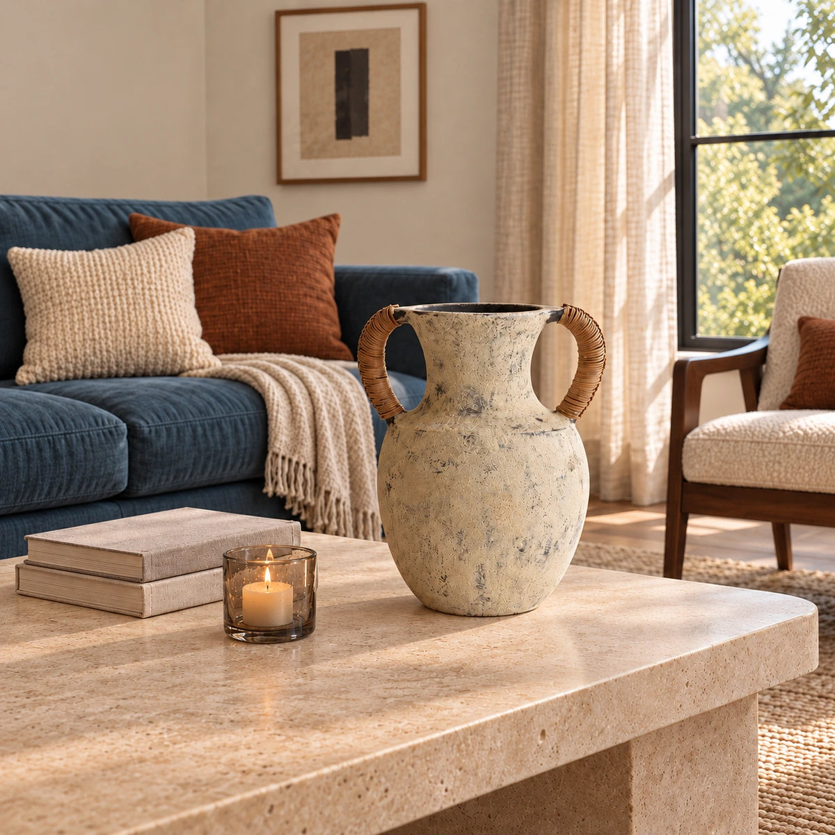 Empty twin-handle ceramic vase on a pale stone coffee table with books, a candle and blue seating