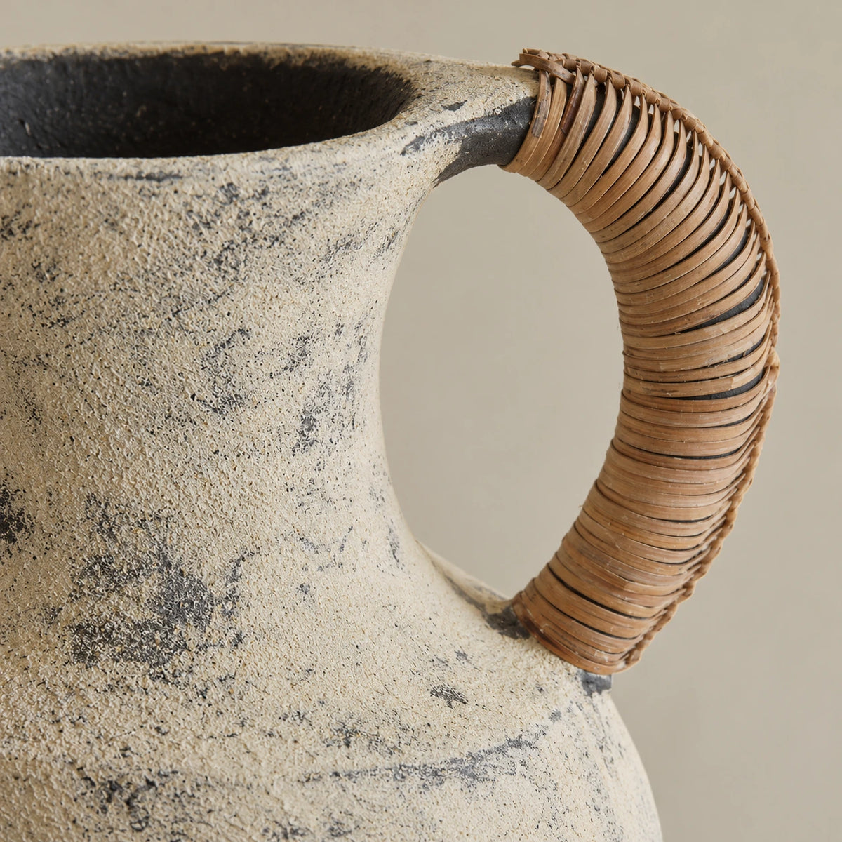 Close view of a brown wrapped handle, dark rim joint and granular beige ceramic surface