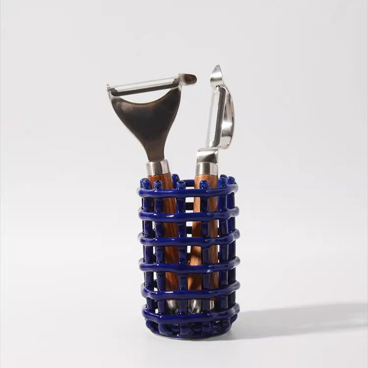 Cobalt blue ceramic lattice caddy holding two vegetable peelers with wooden handles on a white surface.