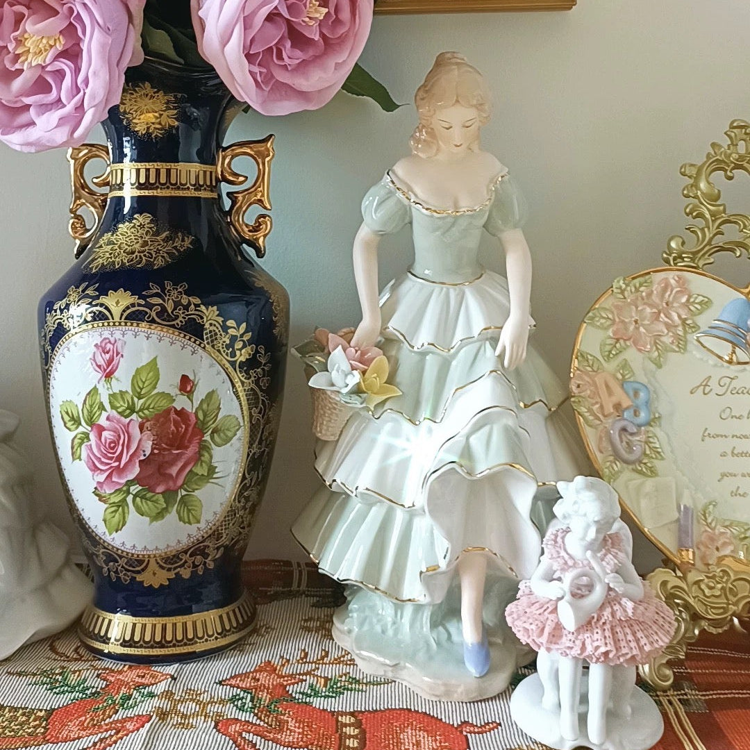Decorative scene with a vase of pink flowers, a figurine, and a framed picture on a table.