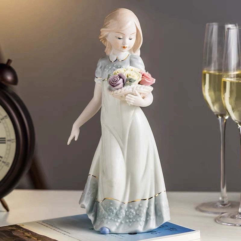 Decorative figurine of a girl holding flowers on a surface with glasses and a clock in the background.