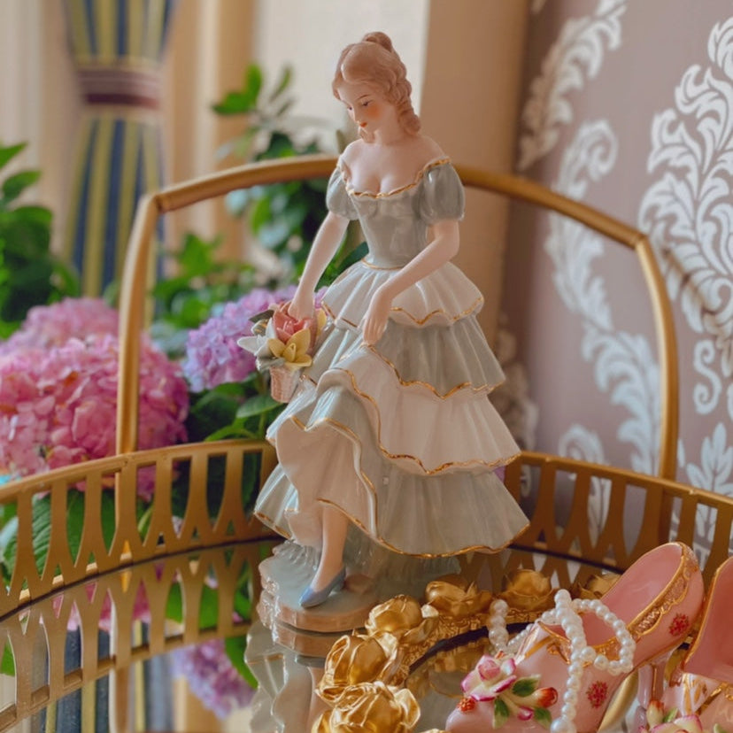 Decorative figurine of a woman in a dress with flowers, placed on a decorative stand with gold elements.
