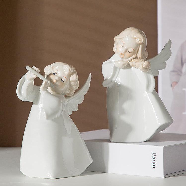 Two white angel figurines on a white surface with a blurred background