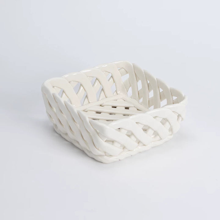 Off-white ceramic square basket with open woven glossy bands and curved corners, shown empty in studio.