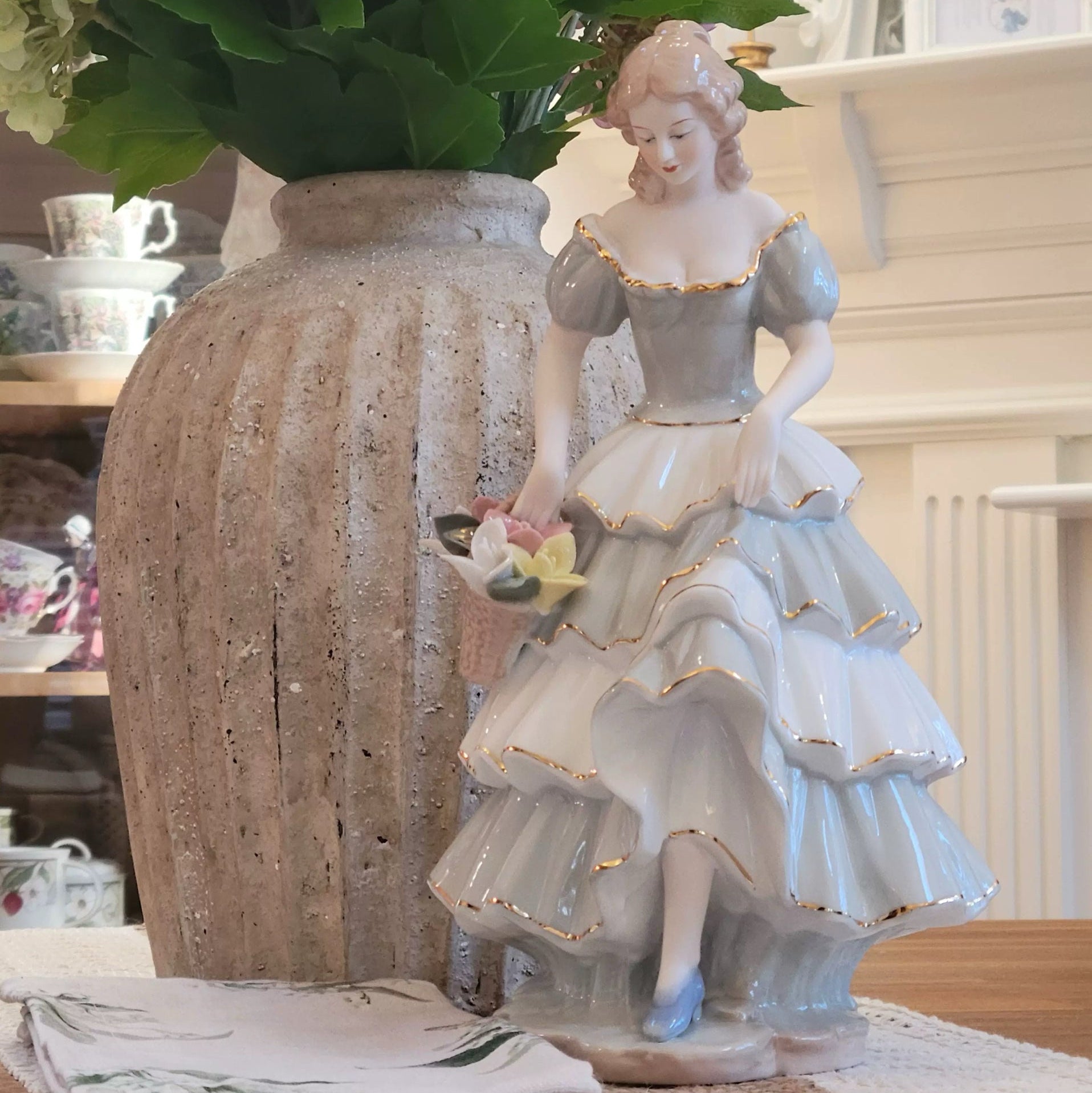 Decorative figurine of a woman in a vintage dress next to a vase with flowers.