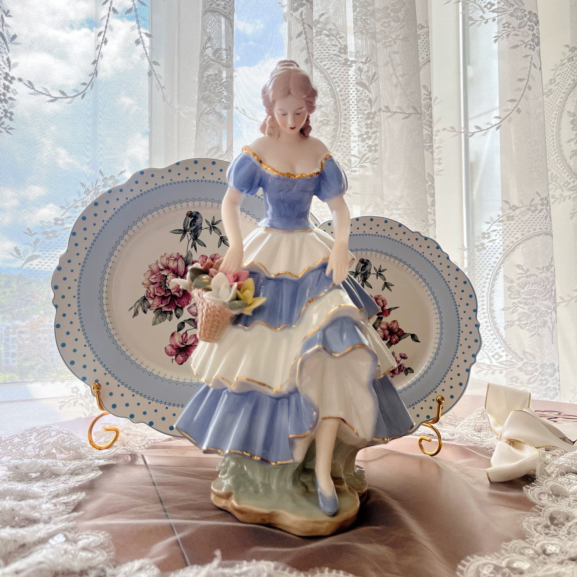 Decorative figurine of a woman holding flowers on a decorative plate with a scenic background.