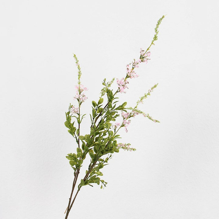 Bundle of faux wildflower stems featuring small pale pink blossoms and dense oval green leaves against a wall.