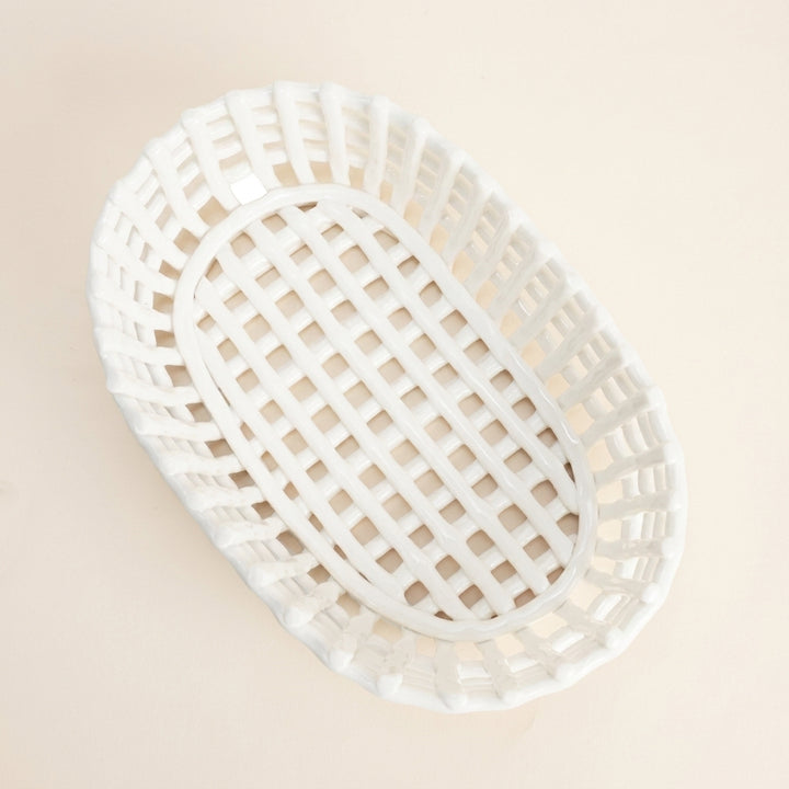 Overhead view of an empty white woven ceramic oval basket with an open lattice base, isolated on a cream background.