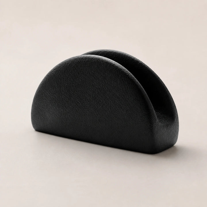 Black ceramic napkin holder with twin rounded arches on a warm neutral background
