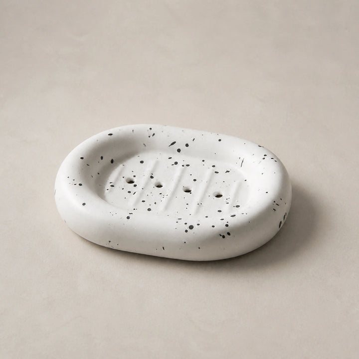 Ink splatter white rounded ceramic soap dish on a light stone background