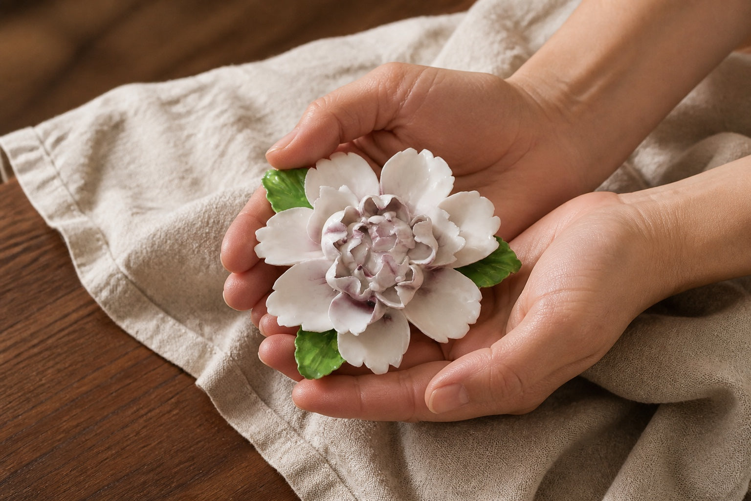 A finished plum-purple ceramic wall flower resting across two adult hands to show its small scale.