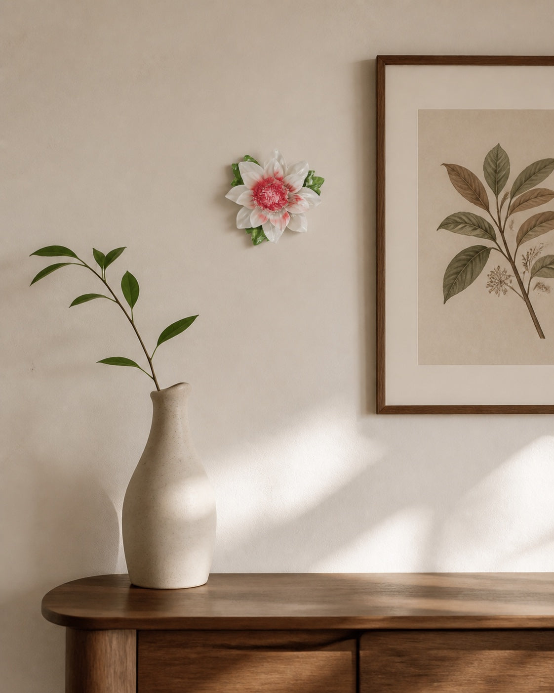 One small rose-red Lotus Bloom ceramic wall flower beside a tall ceramic vase and framed botanical print.