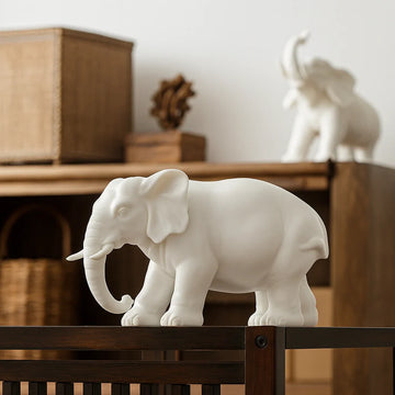 White ceramic elephant figurine on dark wooden table with wicker baskets and shelves in background