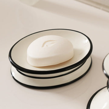 Oval white ceramic soap dish with a glossy black rim holding a white bar of soap