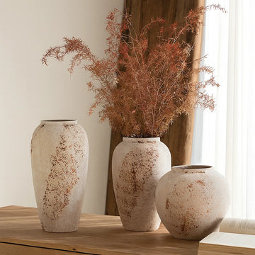 Three distressed off-white ceramic vases with rust-brown patches, one filled with airy dried branches