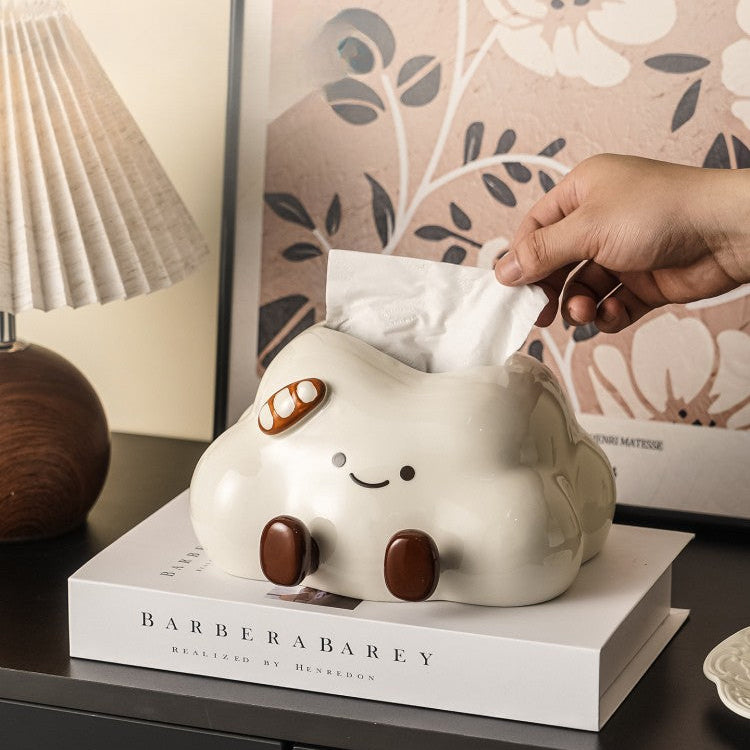 Cute ghost-shaped tissue holder with a hand pulling out a tissue on a table.