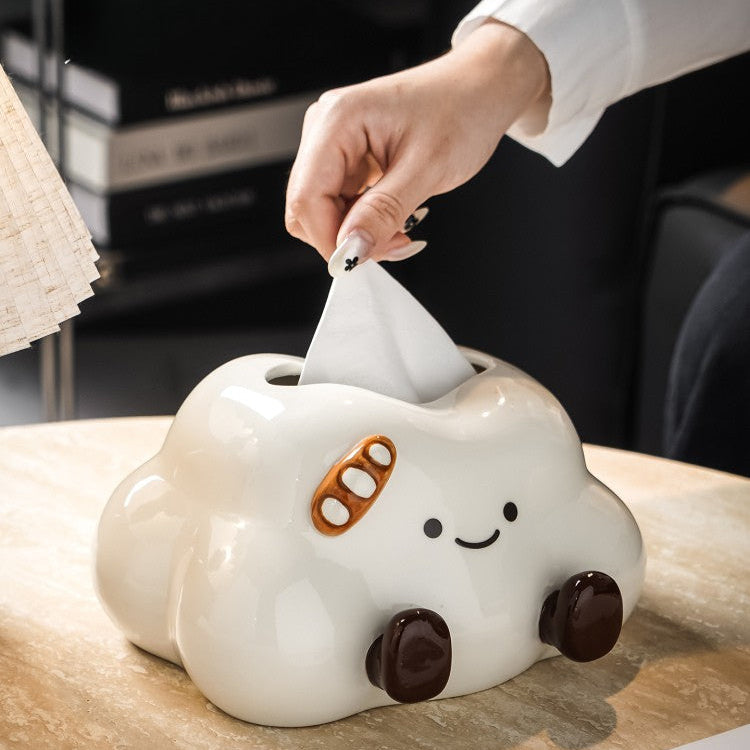 Cloud-shaped tissue box with a smiley face on a wooden surface, with a hand pulling out a tissue.