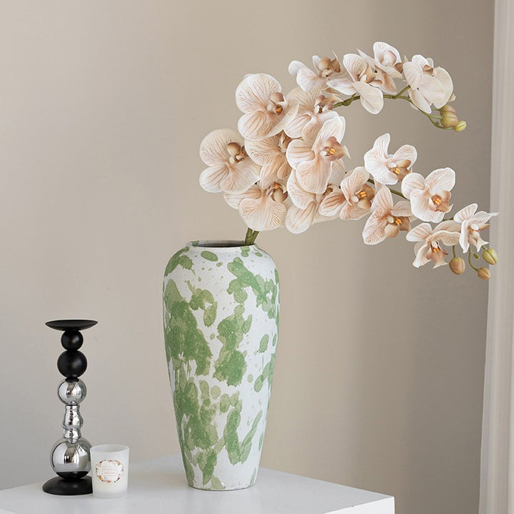 Tall white ceramic vase with a green splatter pattern and pale peach flowers on a white table