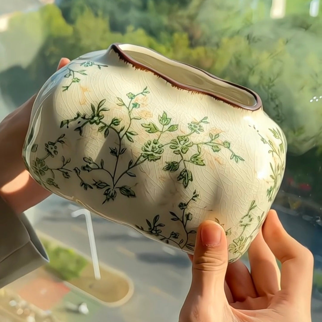 Hand holding a ceramic pot with floral patterns against a blurred green outdoor background
