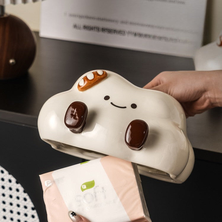 Person holding a cloud-shaped pouch with a smiley face design on a desk.