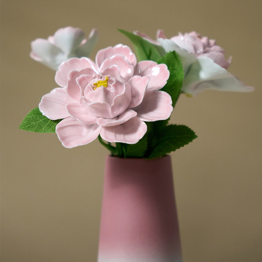 Pink ceramic flower with green leaves on a beige background