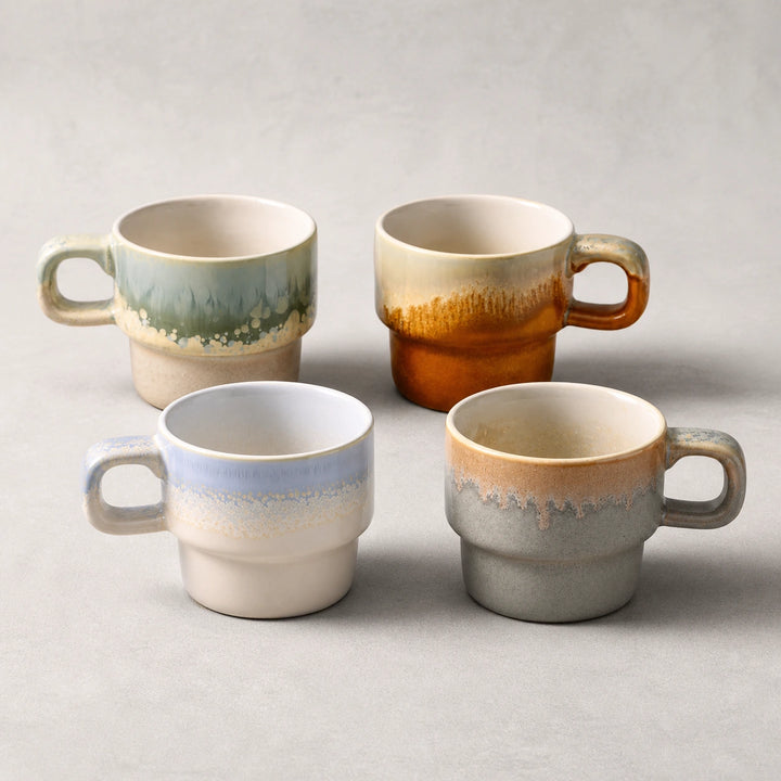 Four-color layered-glaze ceramic mug set on a pearl-gray studio background.