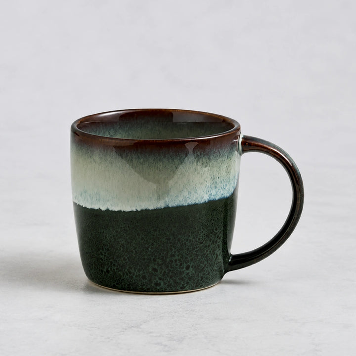 Ink Wash Green ceramic mug with deep green, ivory and brown reactive glaze on a pale background.