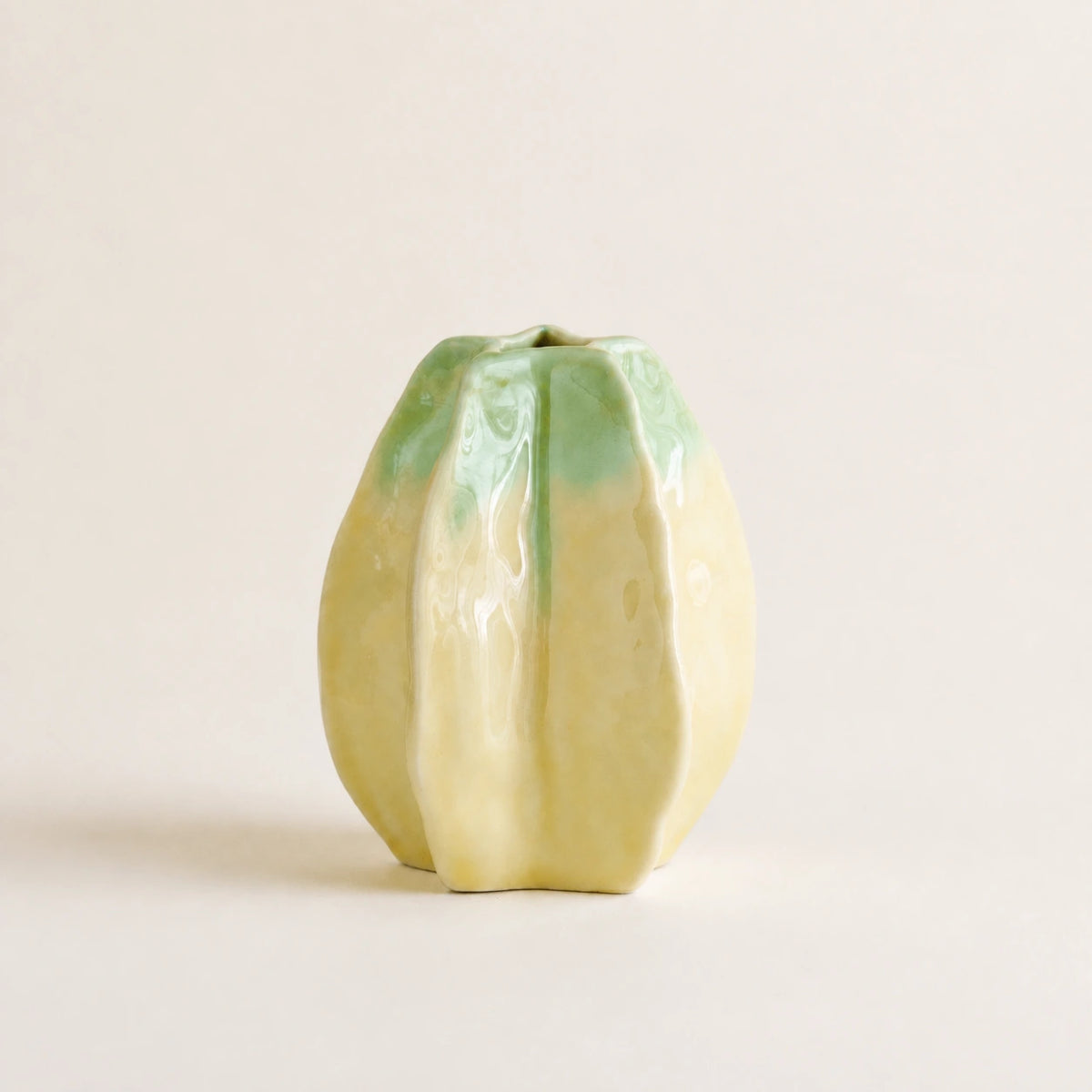 Small starfruit-inspired yellow-green ceramic vase against a warm ivory background.