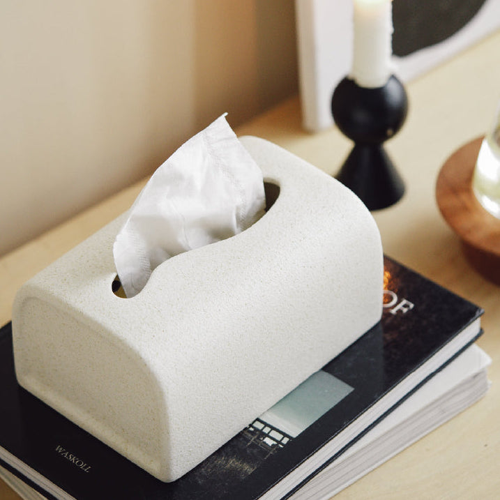 White tissue paper in a stone-like tissue holder on a surface with a candle in the background.