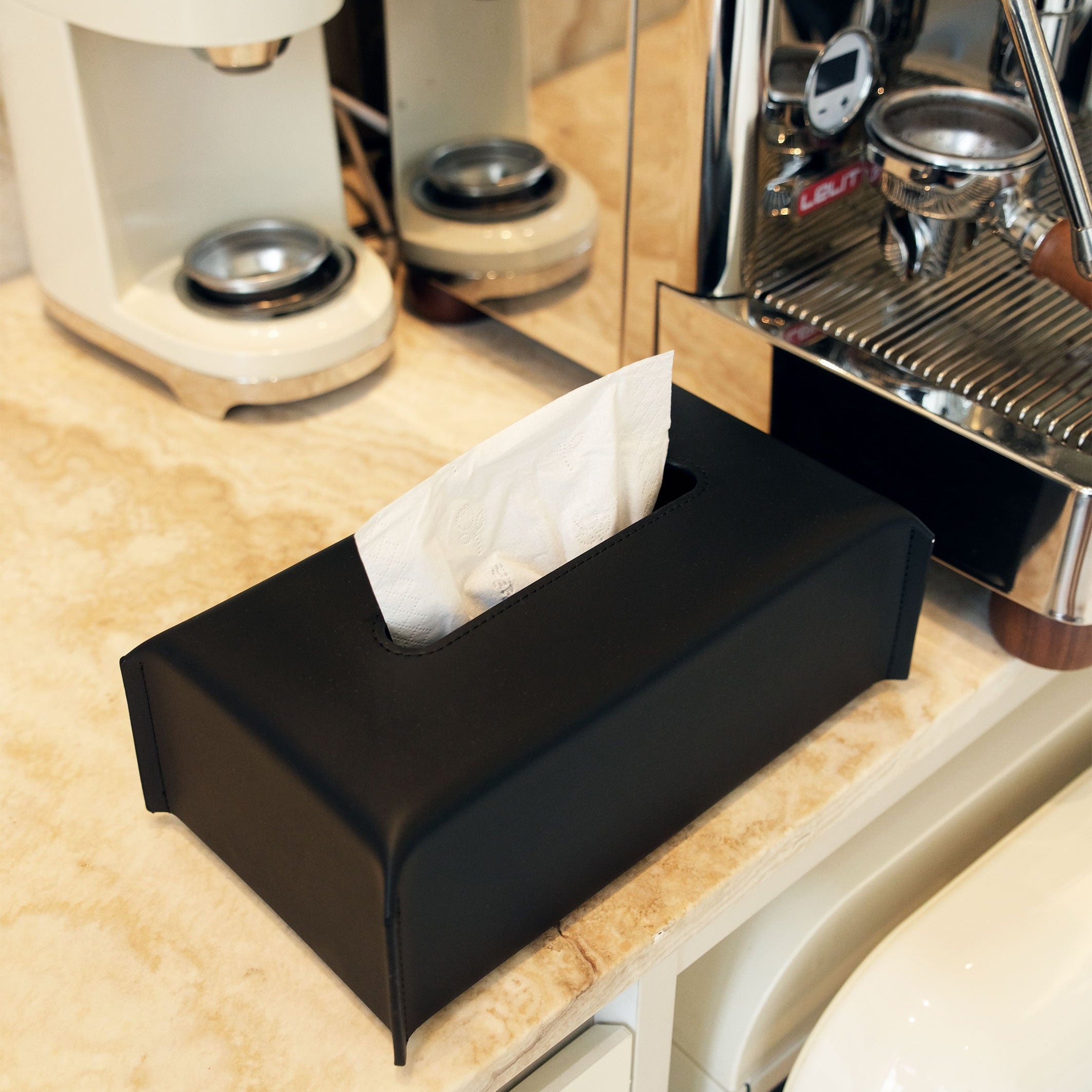 Black tissue box on a kitchen counter with coffee-making equipment in the background