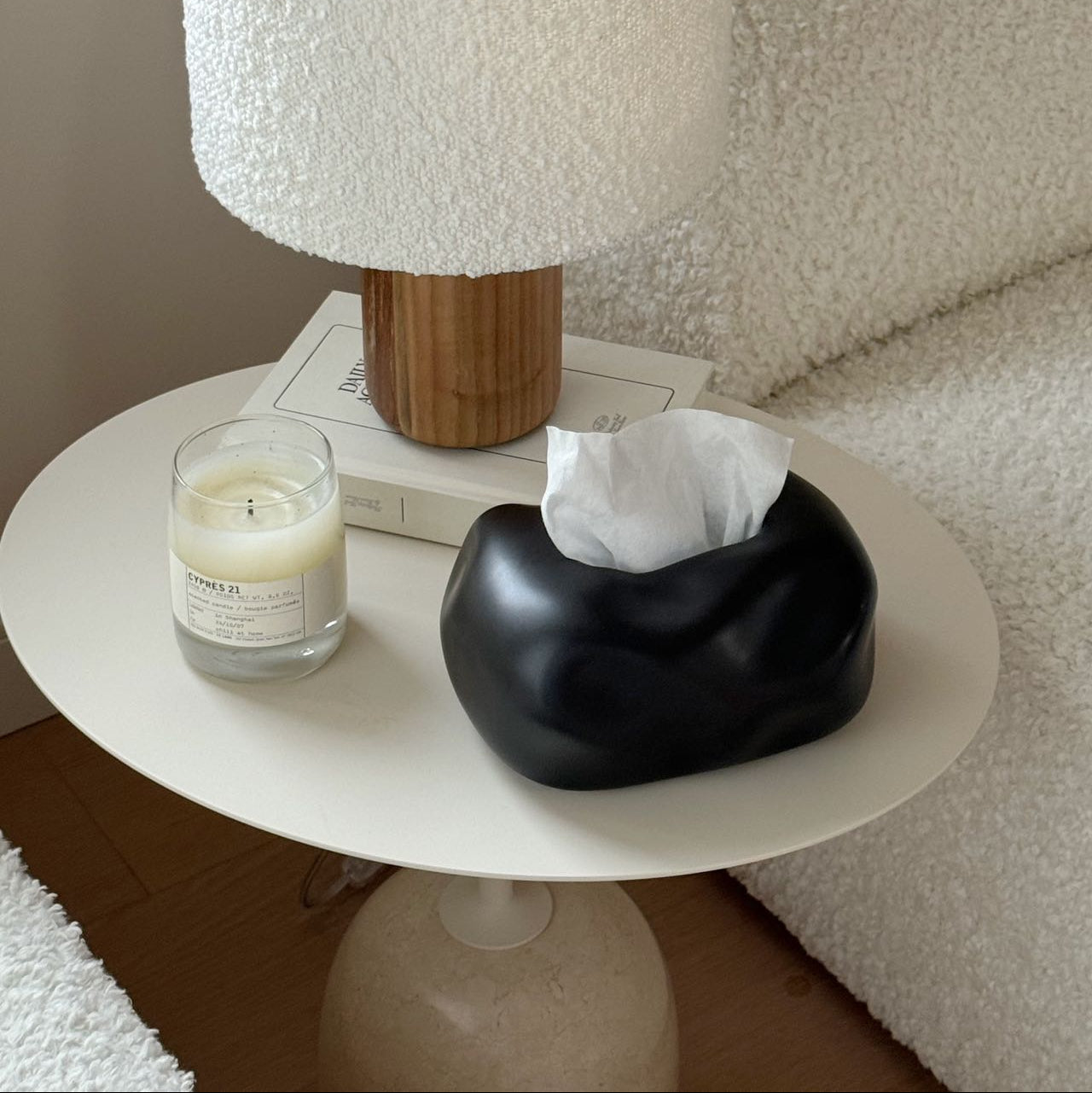 White textured lamp on a small round table with a candle and tissue box.
