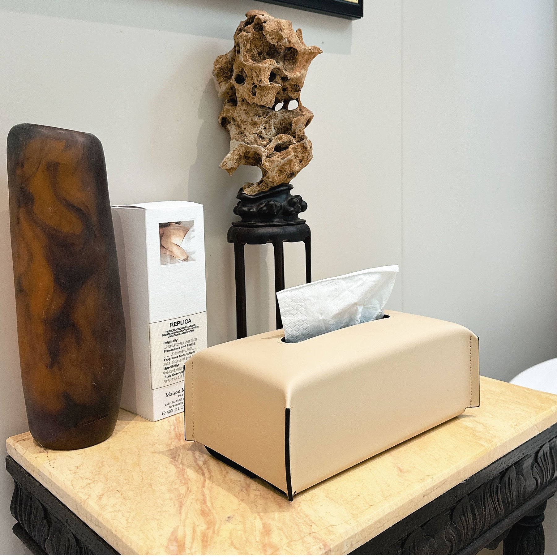 Beige tissue box on a marble surface with decorative items in the background