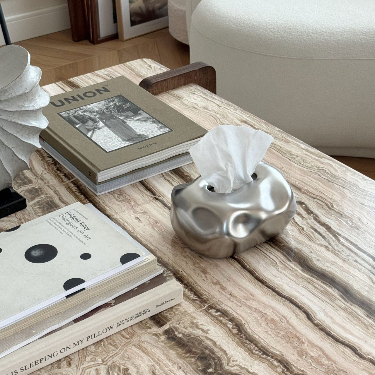 Coffee table with books, a tissue box, and decorative items in a living room setting. #color_silver
