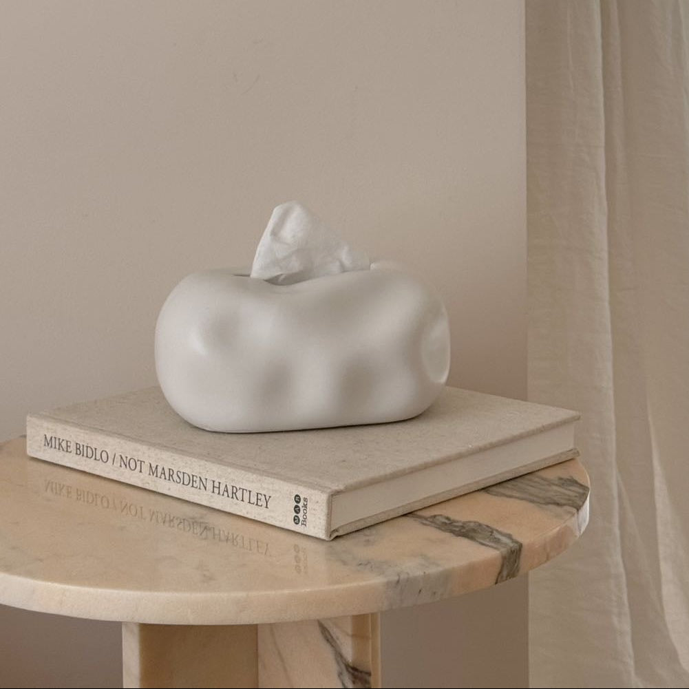 White ceramic sculpture on a book with a window and chair in the background