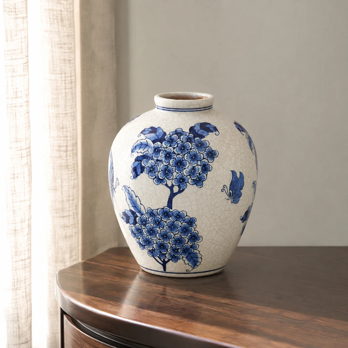 Small blue and white floral vase on a walnut side table beside a linen curtain.