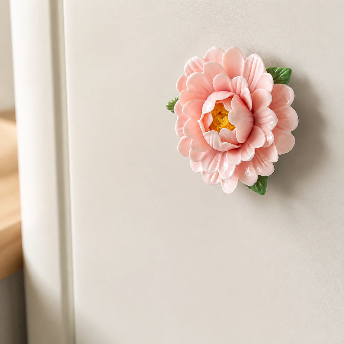 Blush pink ceramic peony refrigerator magnet on a quiet ivory fridge in soft morning light.