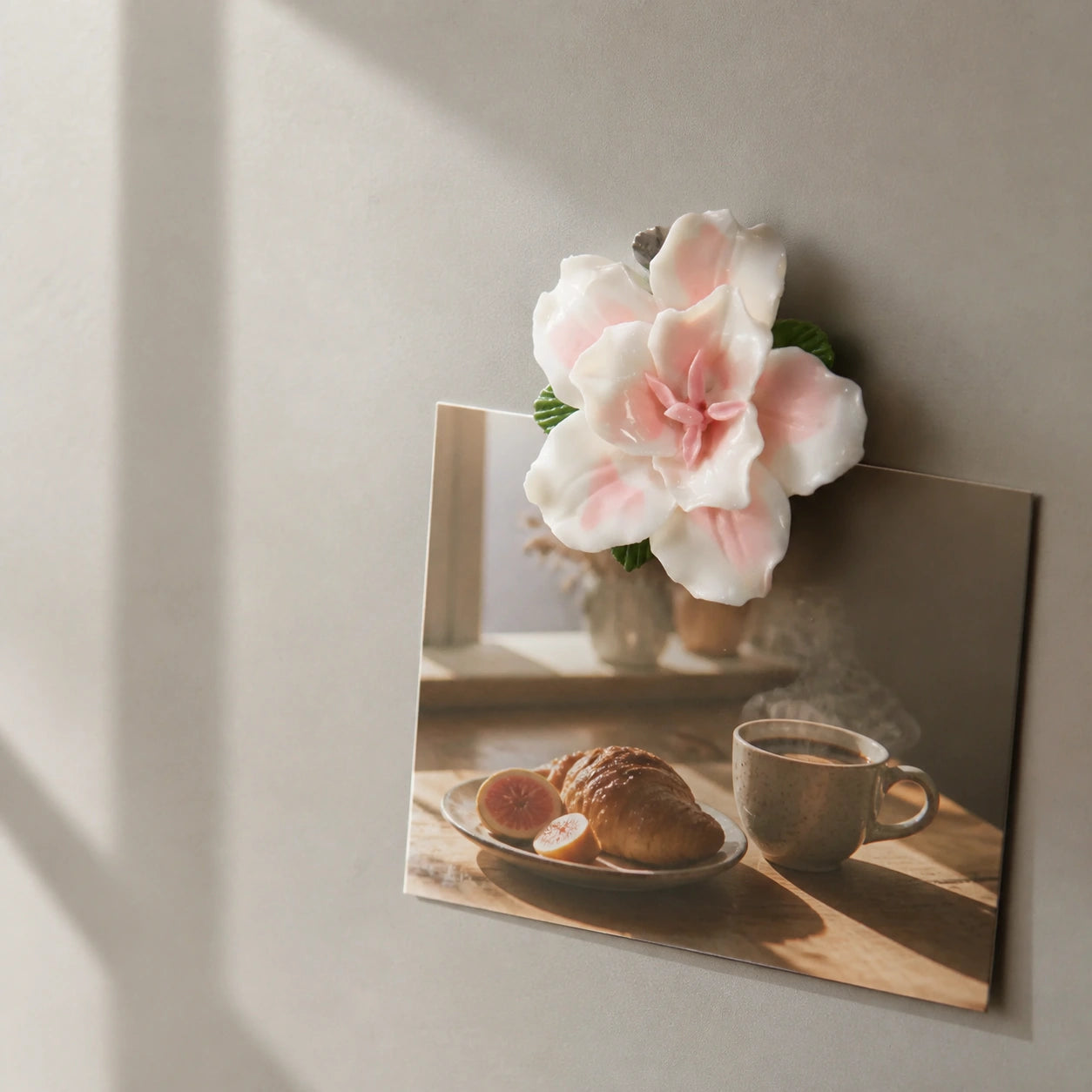 Blush pink ceramic lily magnet holding a warm breakfast photograph on a putty-gray cabinet.
