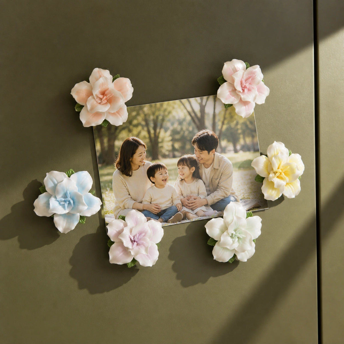 Six-color ceramic lily magnet set arranged around a joyful family photograph on deep olive.
