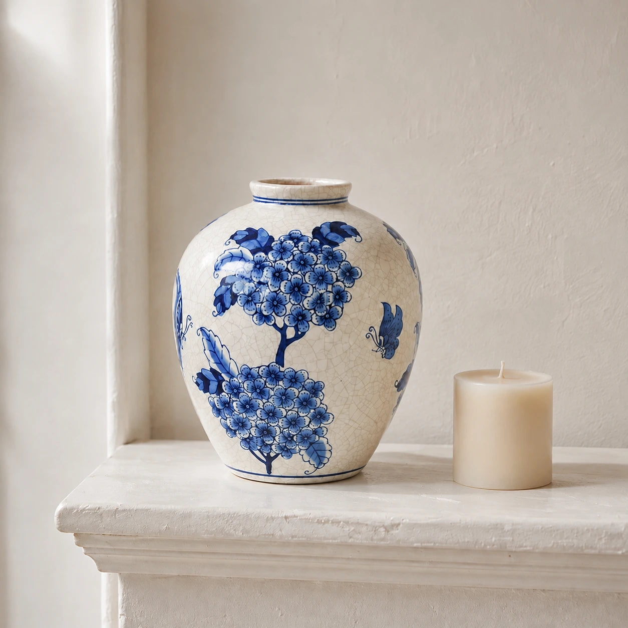 Small blue and white vase beside an unlit ivory candle on a pale mantel.