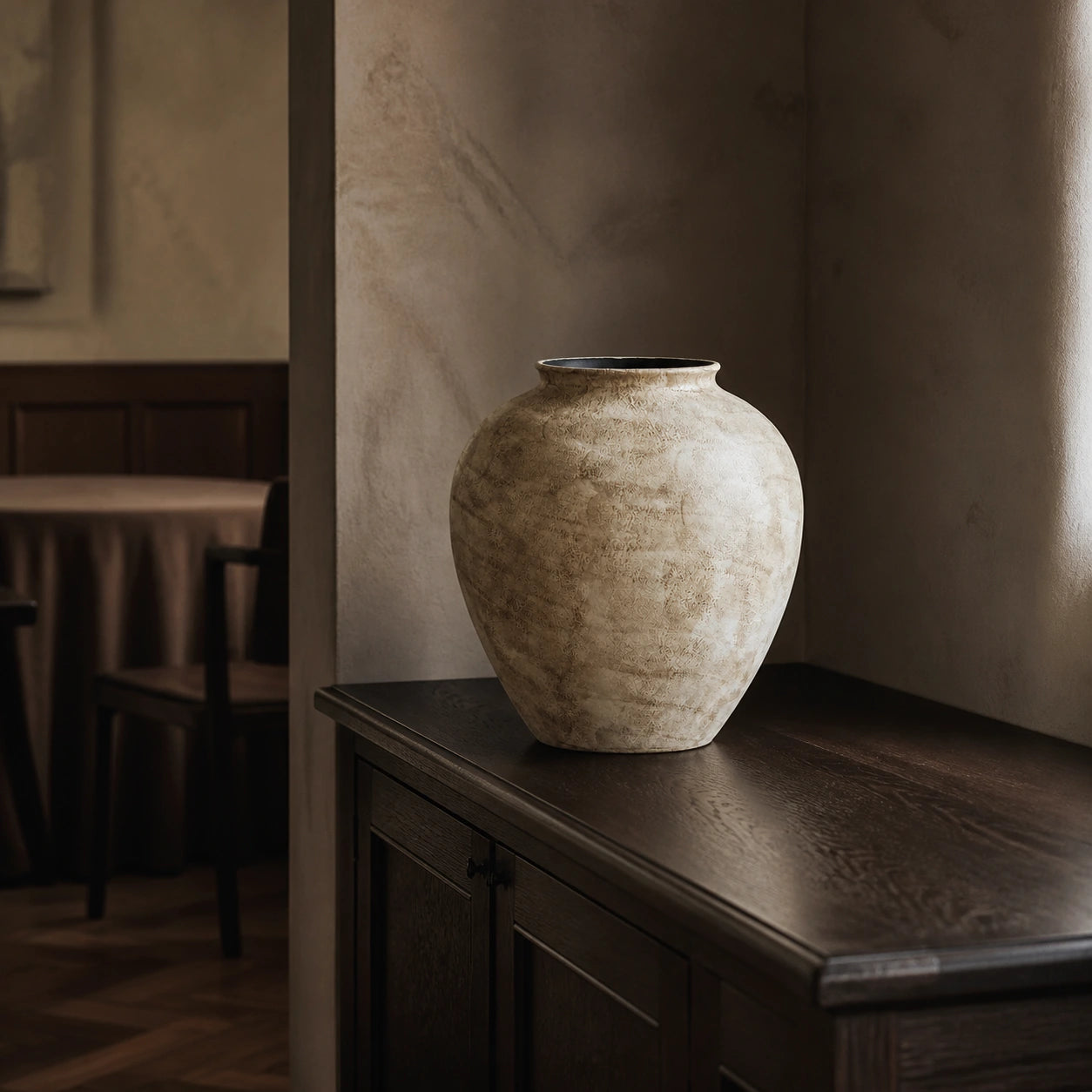 Large stone-textured ivory ceramic vase displayed empty on a dark oak sideboard in an intimate dining alcove.