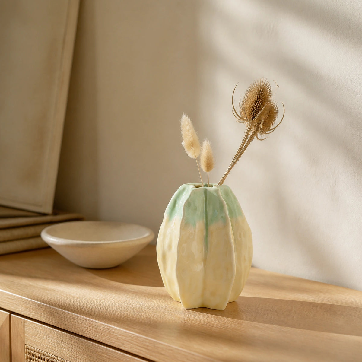 Medium starfruit-inspired ceramic vase displayed with dried stems on a wooden sideboard.