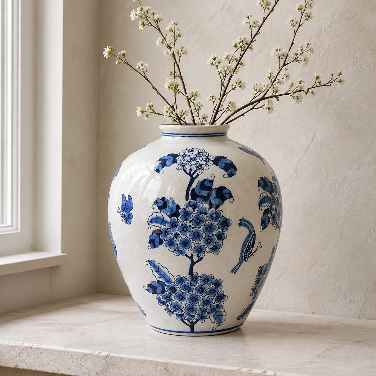 Large blue and white floral vase with white blossom branches on a pale stone ledge.