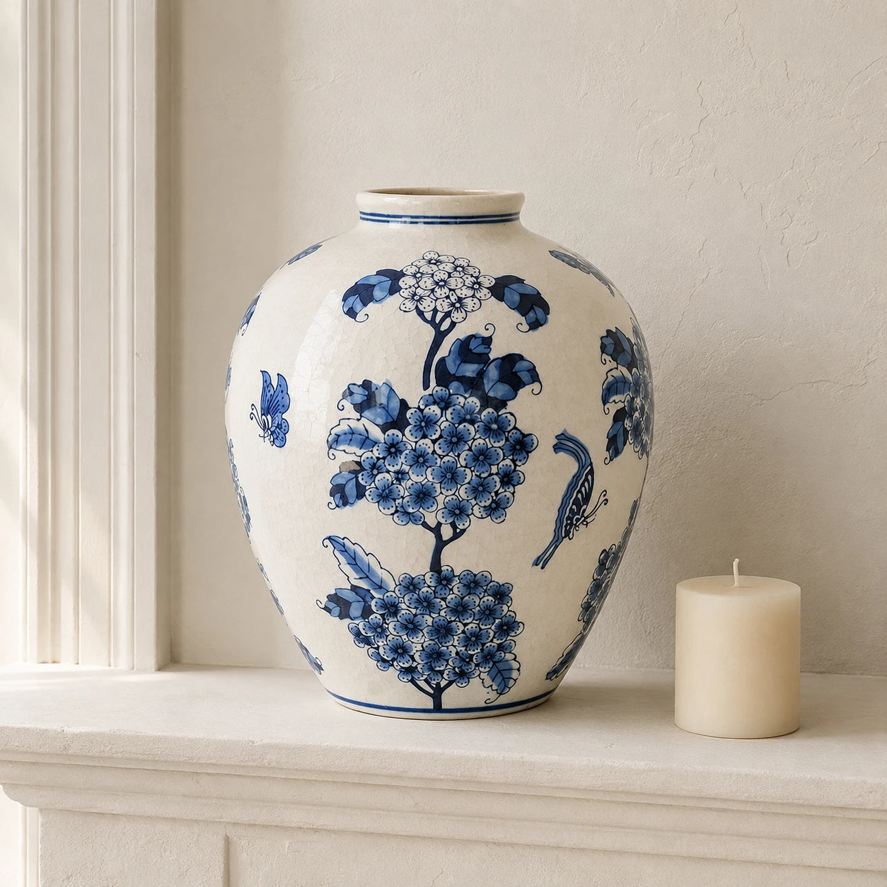 Large blue and white vase beside a short unlit ivory candle on a pale mantel.