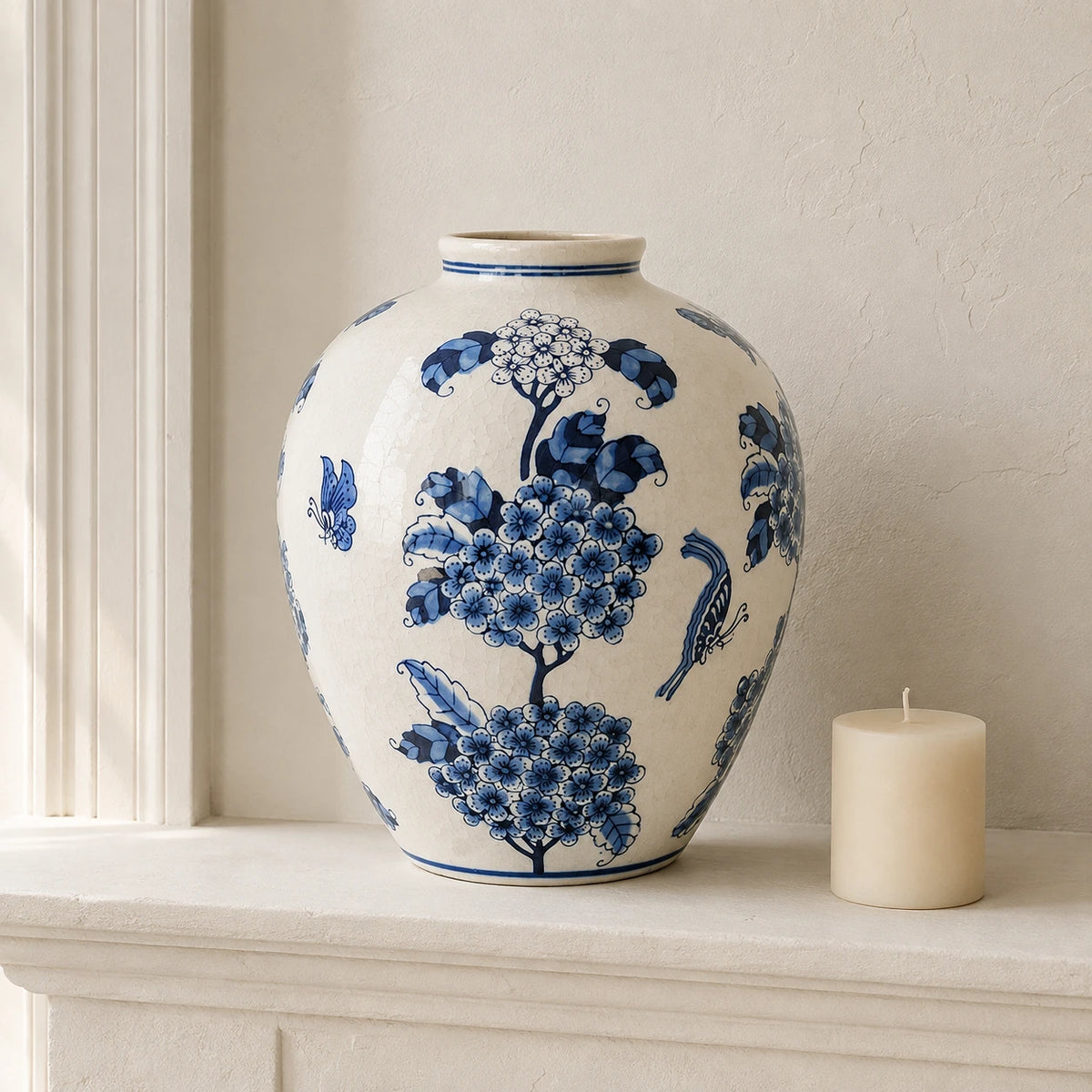 Large blue and white vase beside a short unlit ivory candle on a pale mantel.
