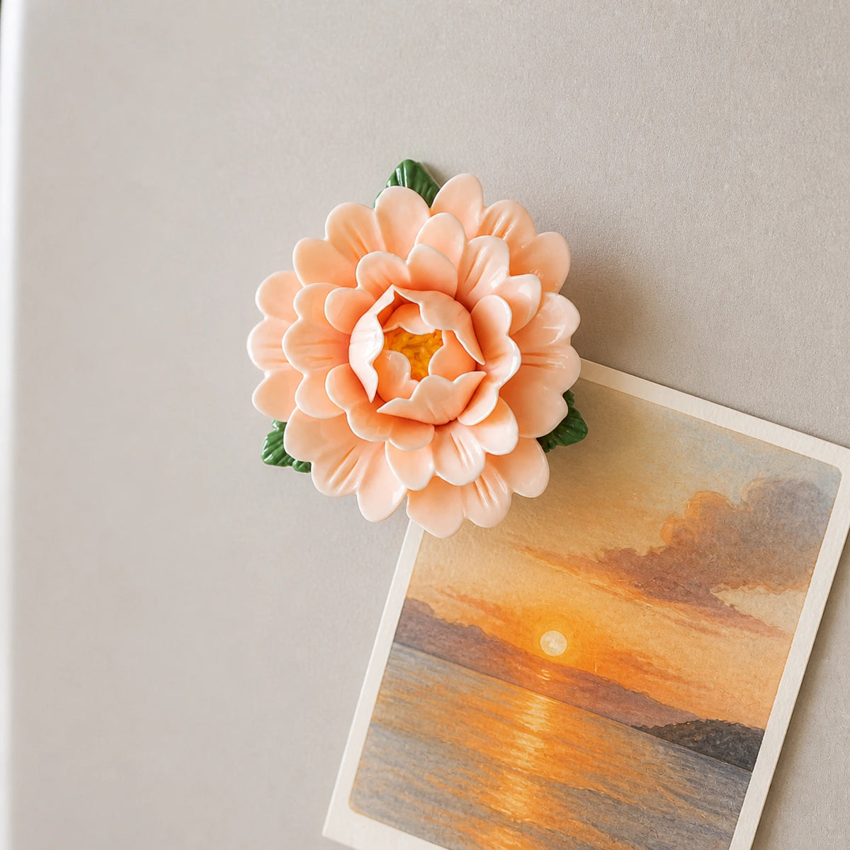 Aimant pivoine en céramique abricot doux retenant une carte illustrée de lever de soleil.