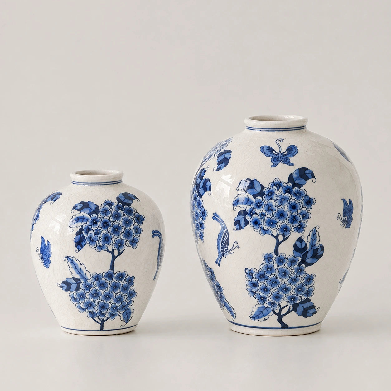 Small and large blue and white floral vases side by side, with a butterfly high on the large vase.