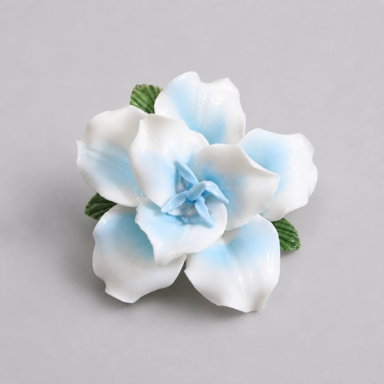 Powder blue glazed ceramic lily refrigerator magnet on a light pearl-gray background.