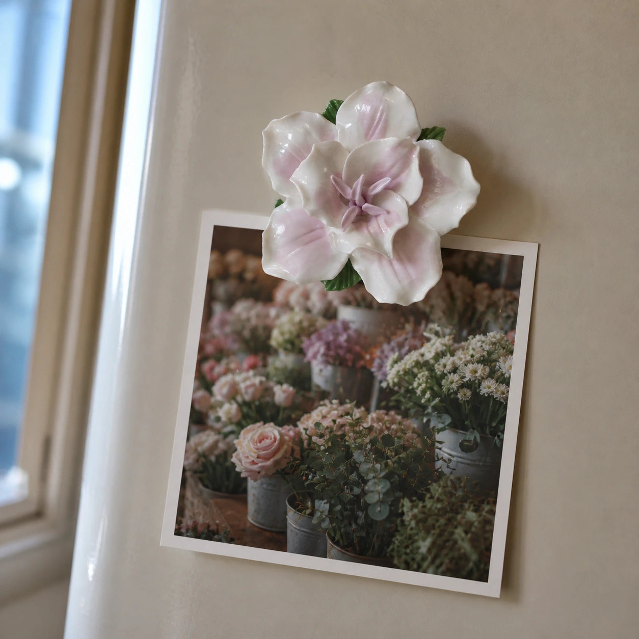 Soft lavender ceramic lily magnet holding a flower-market photograph on warm gray enamel.