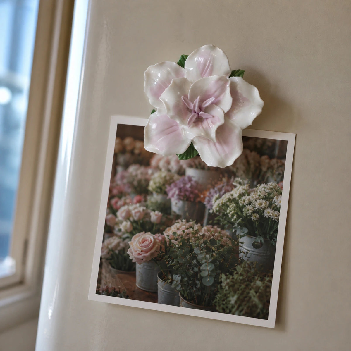 Soft lavender ceramic lily magnet holding a flower-market photograph on warm gray enamel.